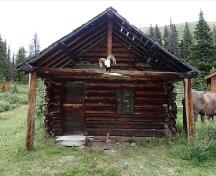 Vue de l'entrée principale du Chalet des gardes du parc du col Divide , qui montre le porche d’entrée couvert décalé par rapport au centre de la structure, 2016.; Steve Malins, Agence Parcs Canada / Parks Canada Agency, 2016.