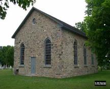 Vue générale de la Vieille-Église-en-Pierre, qui montre la porte centrale de l'entrée placée dans le mur pignon et flanquée de deux grandes fenêtres à vitres multiples, 2006.; Parks Canada Agency / Agence Parcs Canada.