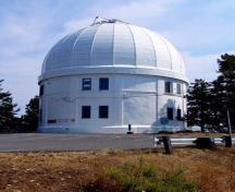 General view of the Dominion Astrophysical Observatory showing its simple cylindrical massing with dome.; Parks Canada / Agence Parcs Canada, Andrew Waldron.