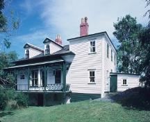 Rear facade showing its deep verandah on three sides with bellcast roof and decorative wooden fretwork, and its generous bay and French windows.; Parks Canada Agency / Agence Parcs Canada