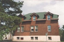 Façade latérale de l'édifice Arc Biotech (no 34); qui montre le motif subtil de bandeau sur les murs en brique rouge, la garniture de bois peint et le soubassement en béton surélevé, 1999.; Agence Parcs Canada / Parks Canada Agency, 1999.
