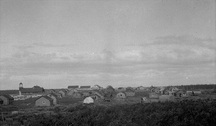 Photo historique du fort McPherson montrant des habitations et l'église anglicanne à la gauche de l'image, toujours en place, vers 1930.; J. F. Moran / Indian and Northern Affairs Canada | Affaires indiennes et du Nord Canada / Library and Archives Canada | Biliothèque et Archives Canada, a102490-v8